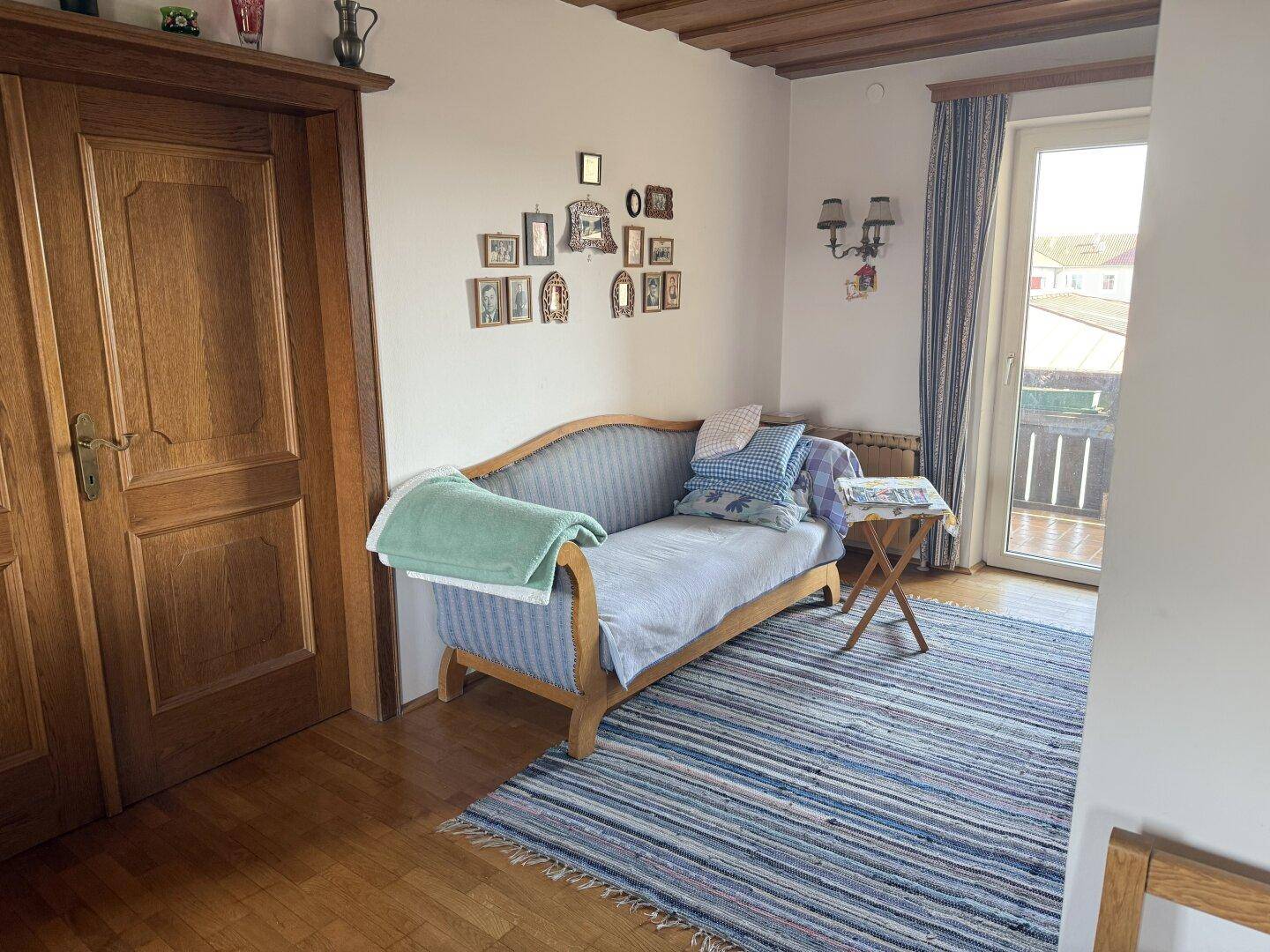 Gemütliches Wohnzimmer mit Holzdecke, Sofa und Zugang zu einem Balkon, dekoriert mit persönlichen Bildern.