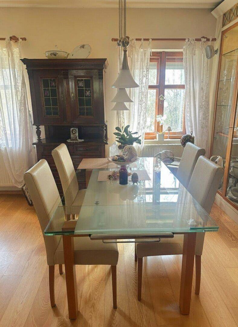 Klassischer Essbereich mit einem Glastisch, bequemen Stühlen und einem antiken Holzschrank.