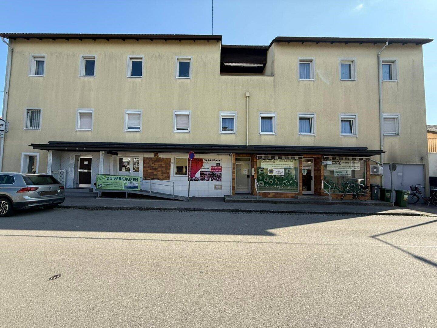Gebäudefassade mit mehreren Fenstern und Geschäften im Erdgeschoss, an einer Straße gelegen.