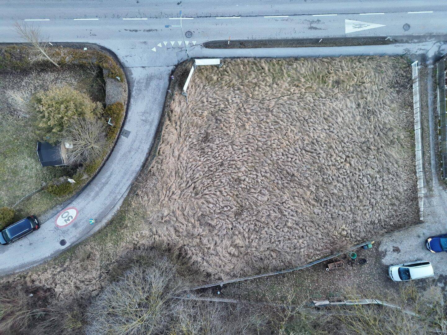 Luftaufnahme eines Grundstücks mit trockener Vegetation neben einer Straße und parkenden Autos.