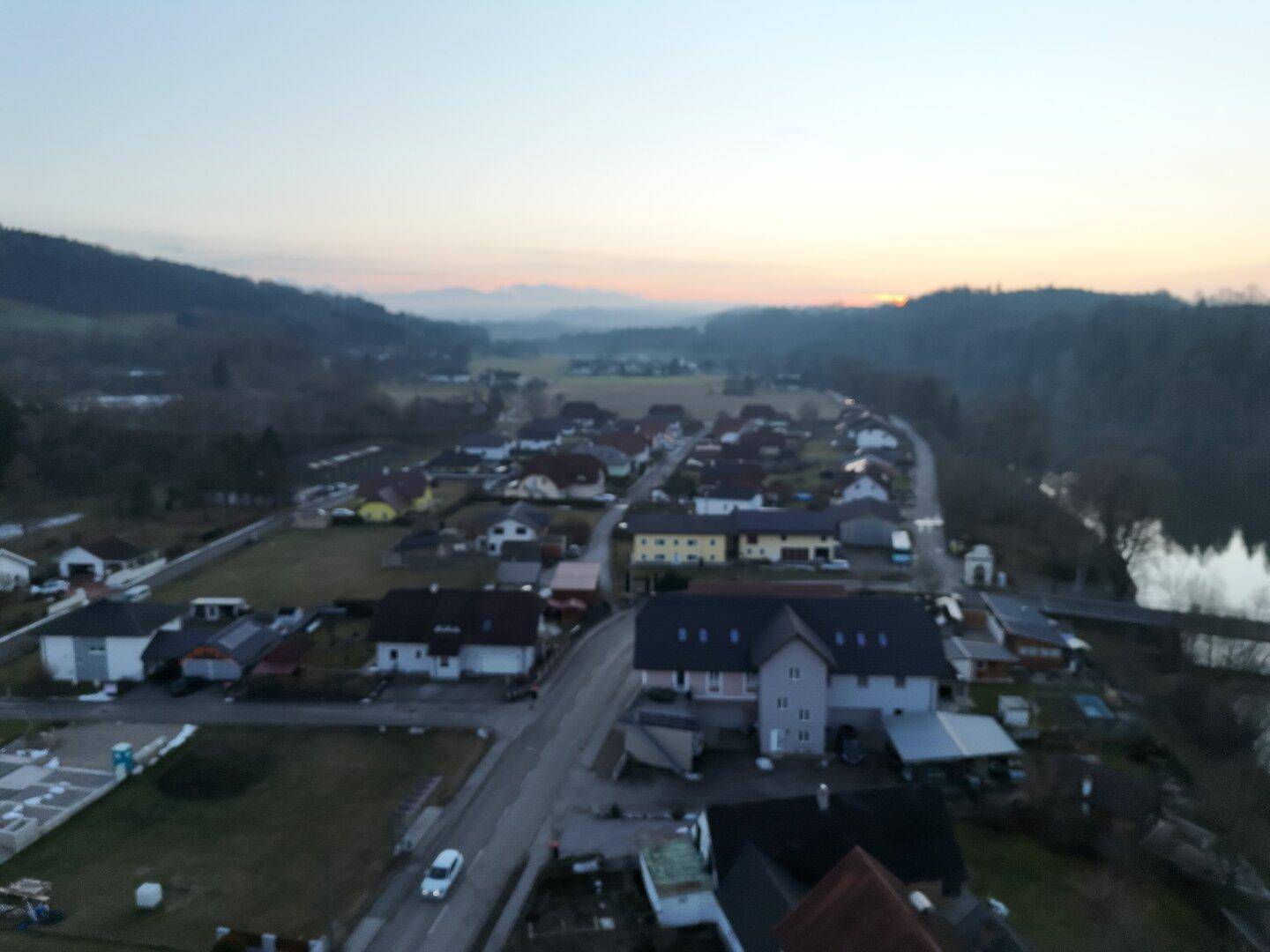 Panoramablick aus der Luft auf ein Dorf bei Sonnenuntergang mit Häusern, Straßen und Bergen im Hintergrund.