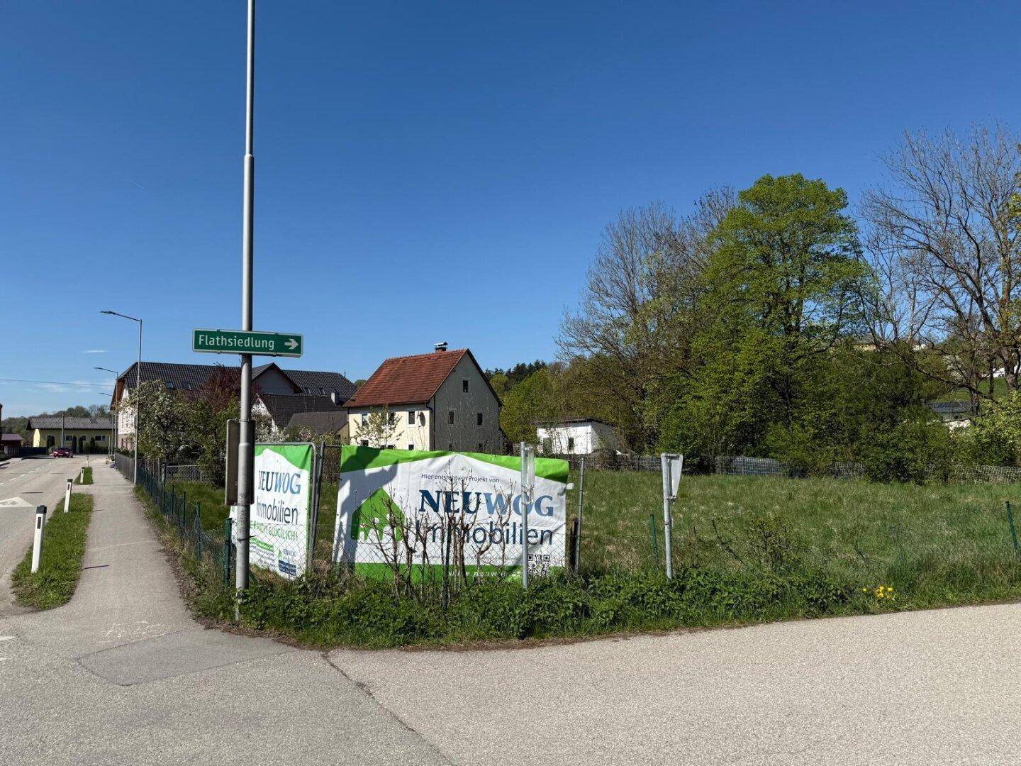 Grundstück an einer Straßenecke mit Werbeschildern für Neubauprojekte und umliegenden Häusern.