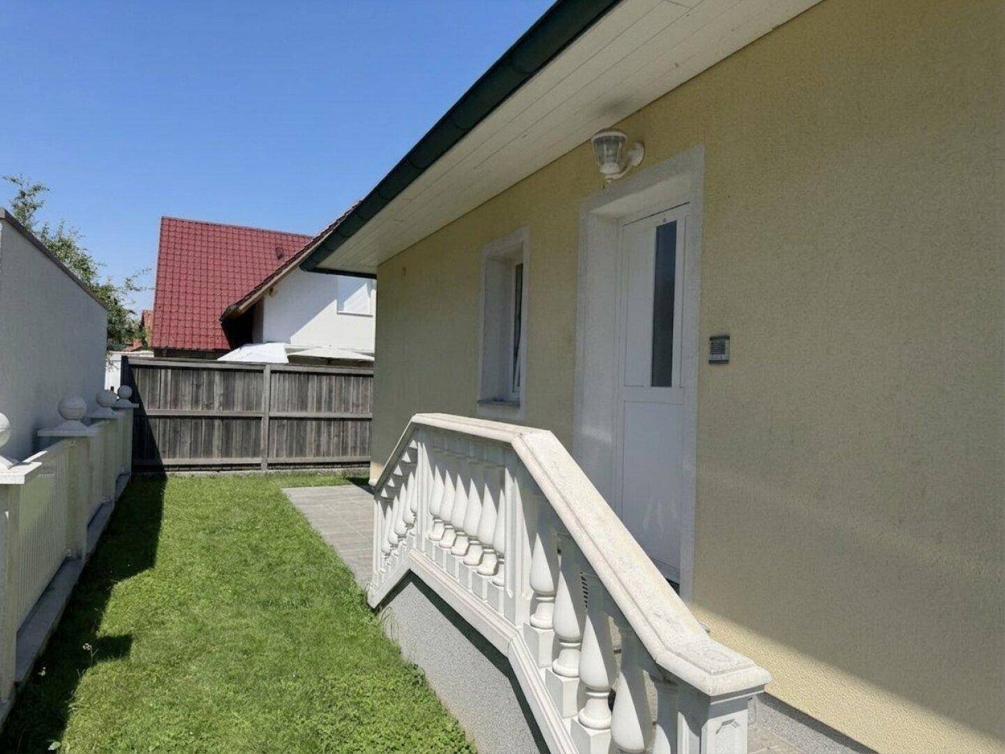 Seitenansicht des Hauses mit Eingangstür, kleiner Treppe und gepflegtem Rasenstreifen.