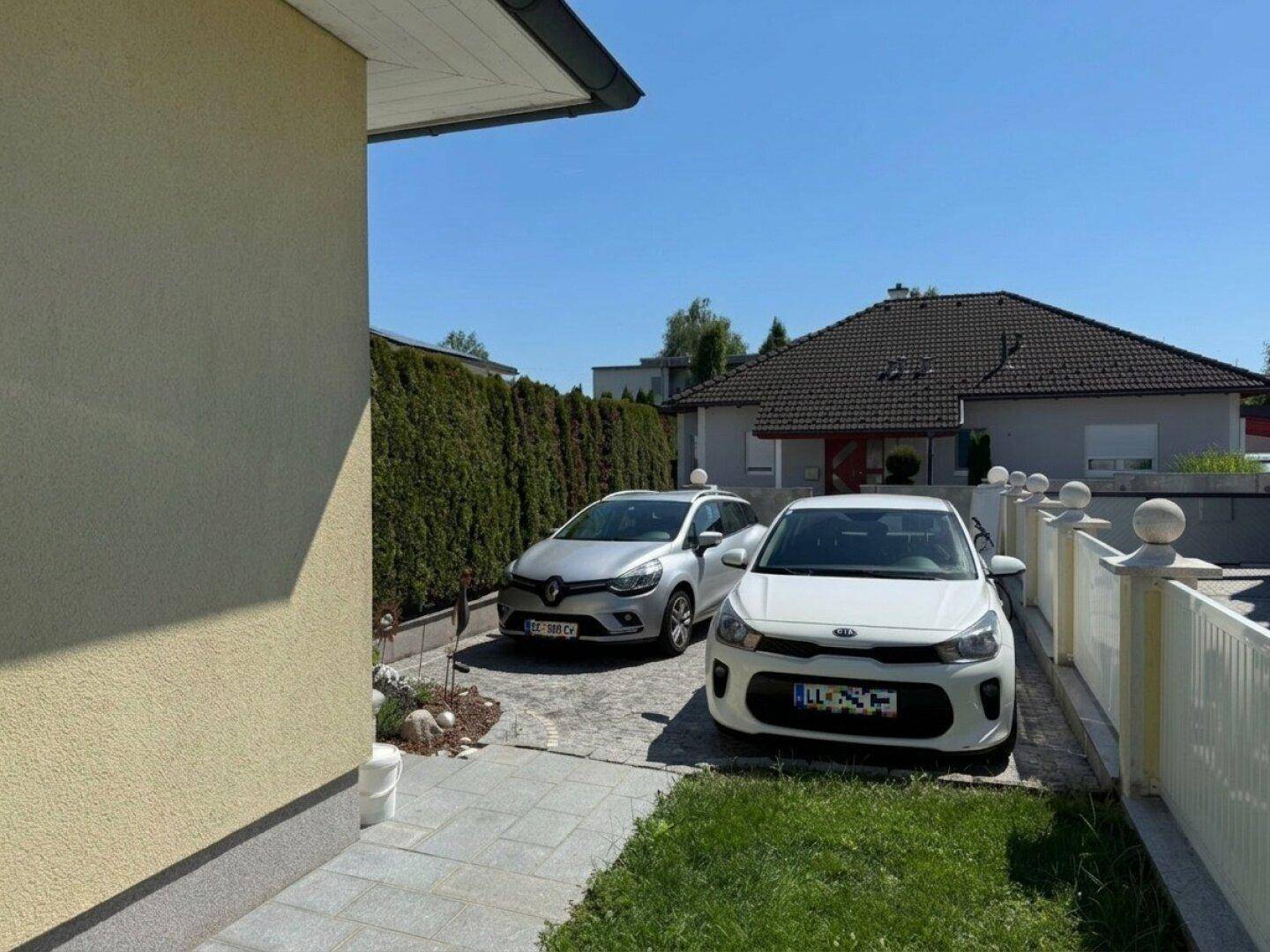 Gepflasterte Einfahrt mit zwei Autos und einer hohen Hecke, die Privatsphäre bietet.