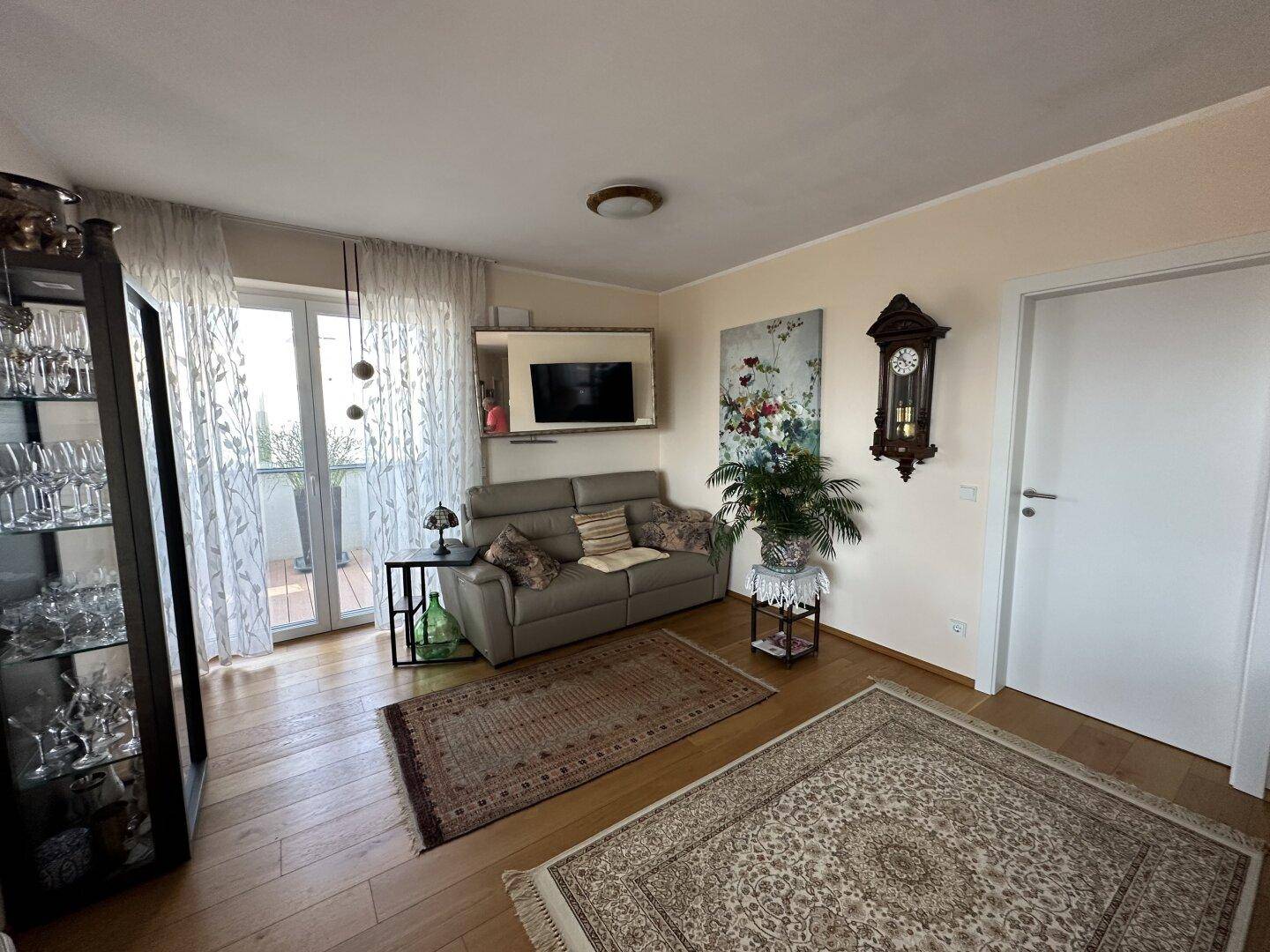 Gemütliches Wohnzimmer mit Holzboden, beigem Sofa, Teppichen und Balkonzugang.