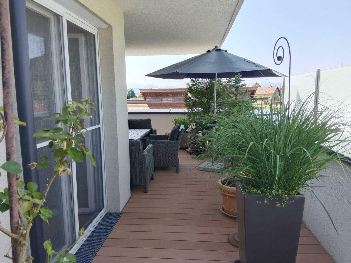 Heller Balkon mit Sonnenschirm, hohen Gräsern in Töpfen und Zugang zum Innenbereich.