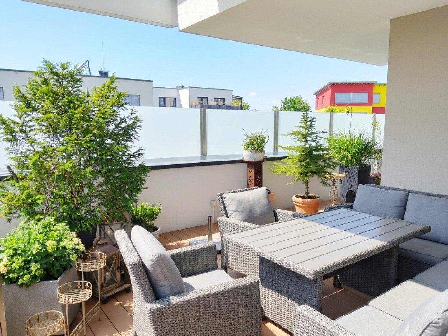 Geräumige Terrasse mit bequemen Sitzmöbeln, vielen Pflanzen und moderner Glasbrüstung.