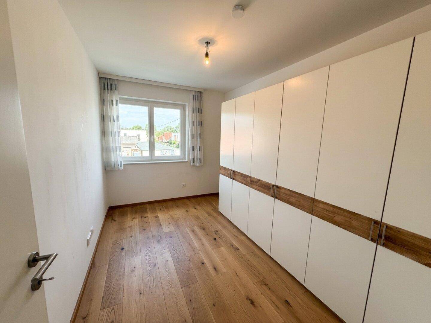 Helles Zimmer mit großem Einbauschrank, Holzboden und einem Fenster für viel Tageslicht.