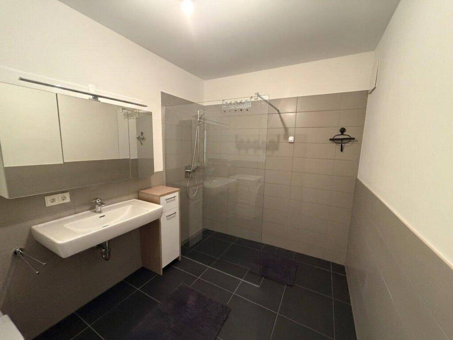 Modernes Badezimmer mit ebenerdiger Dusche, Einzelwaschbecken und grauen Fliesen.