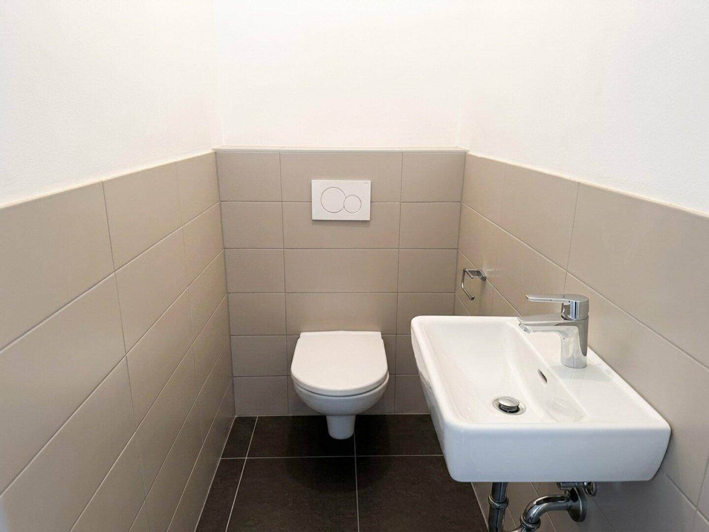 Modernes Gäste-WC mit Wand-WC, kleinem Waschbecken und hellen Fliesen an den Wänden.