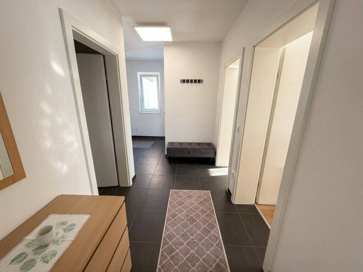 Heller Flur mit dunklen Fliesen, einer Garderobe und Zugang zu verschiedenen Zimmern.