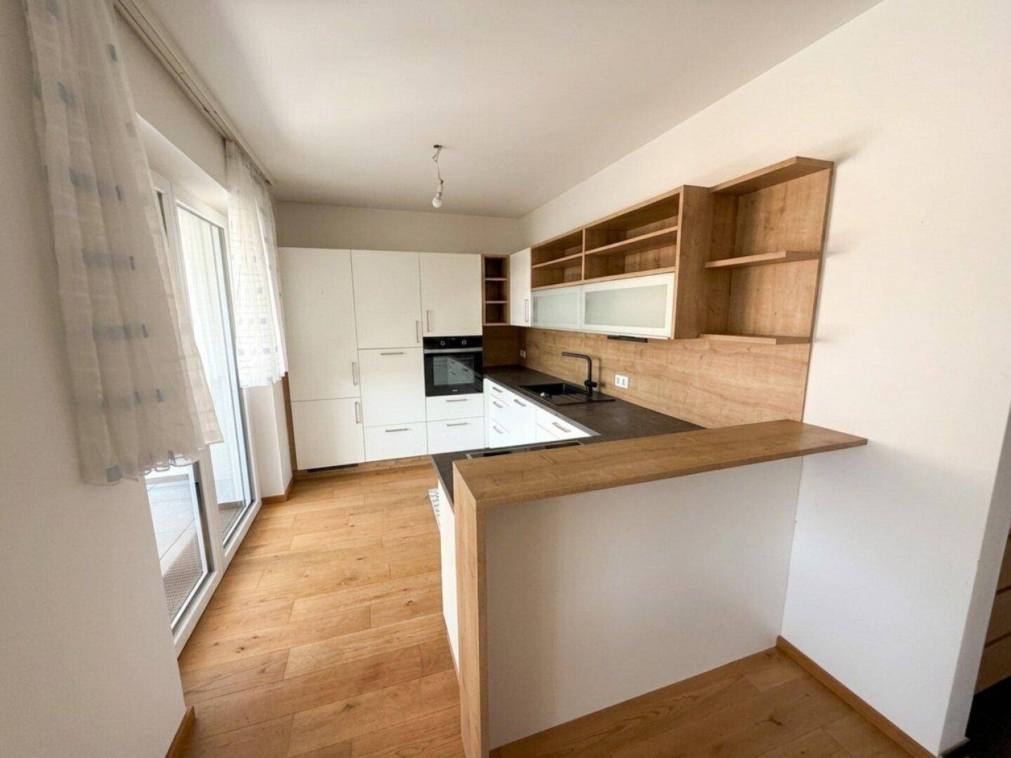 Moderne Küche mit weißen Schränken, Holzakzenten und Zugang zu einem sonnigen Balkon.