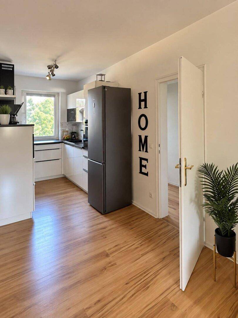 Geräumige Küche mit freistehendem Kühlschrank, weißen Schränken und hellem Laminatboden.