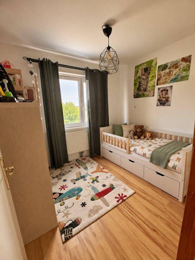 Kinderzimmer mit Einzelbett, farbenfrohem Teppich und Fenster für eine helle Atmosphäre.