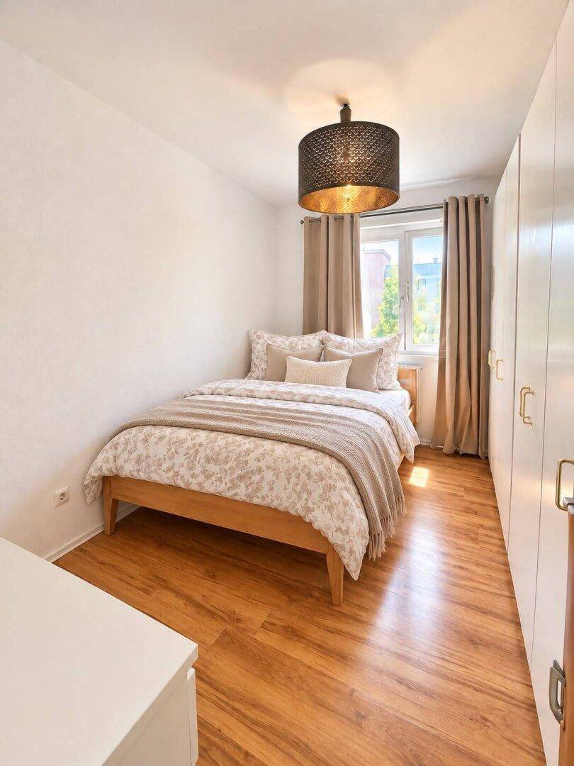 Gemütliches Schlafzimmer mit Doppelbett, Kleiderschrank und Fenster für natürliches Licht.