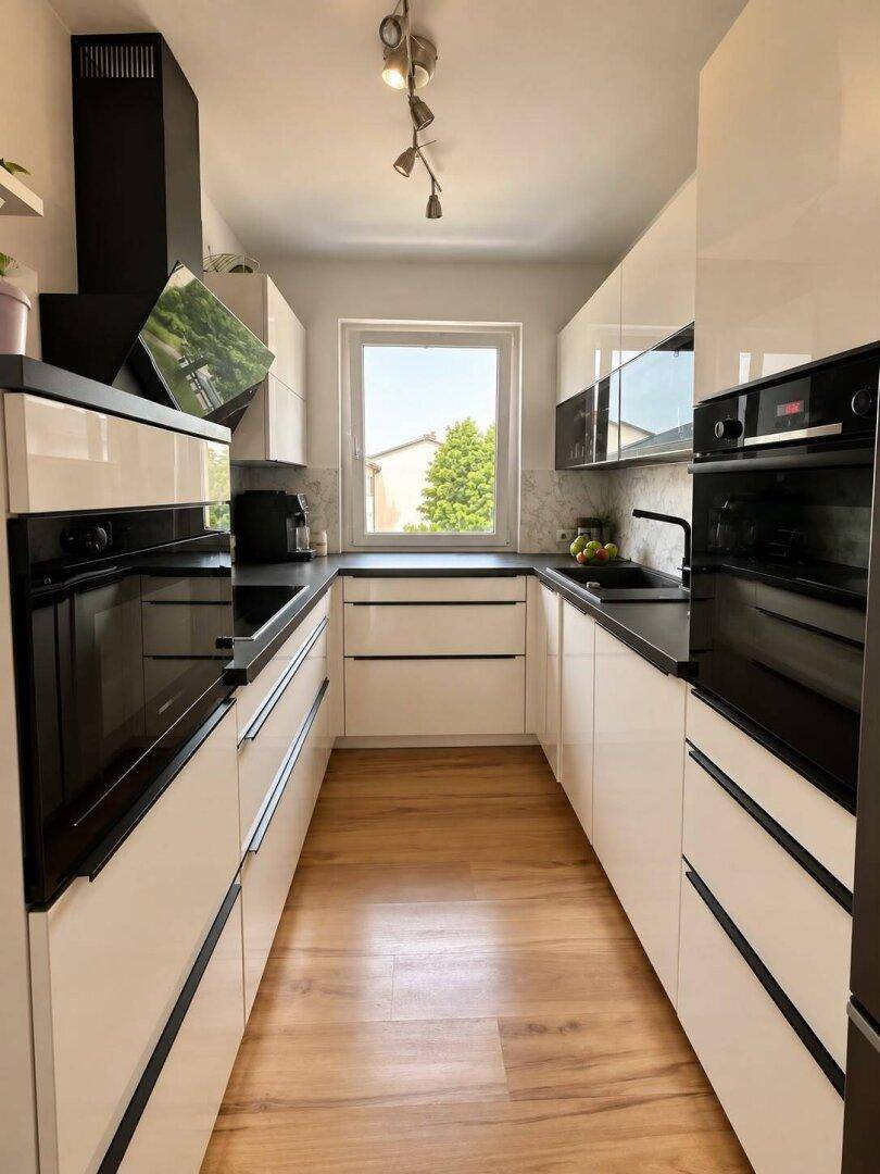 Moderne weiße Küche mit Hochglanzfronten, schwarzen Arbeitsplatten und integrierten Backöfen.
