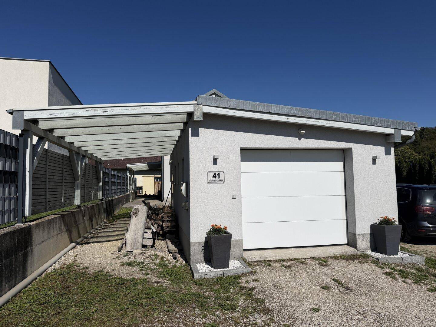 Einzelgarage mit weißem Tor und angrenzendem Carport für zusätzlichen Wetterschutz.
