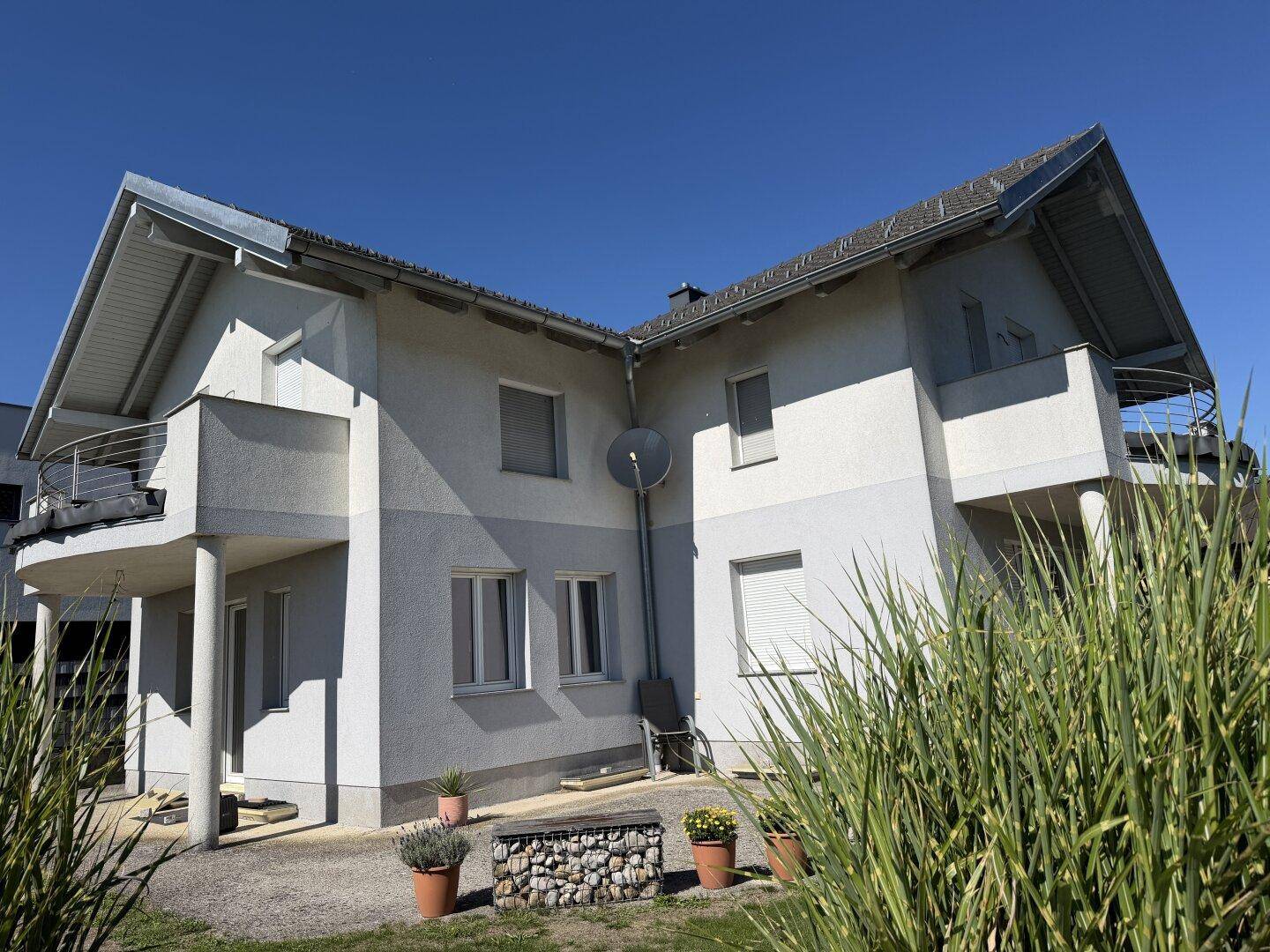 Seitenansicht des Hauses mit mehreren Balkonen und einer kleinen gepflasterten Fläche.