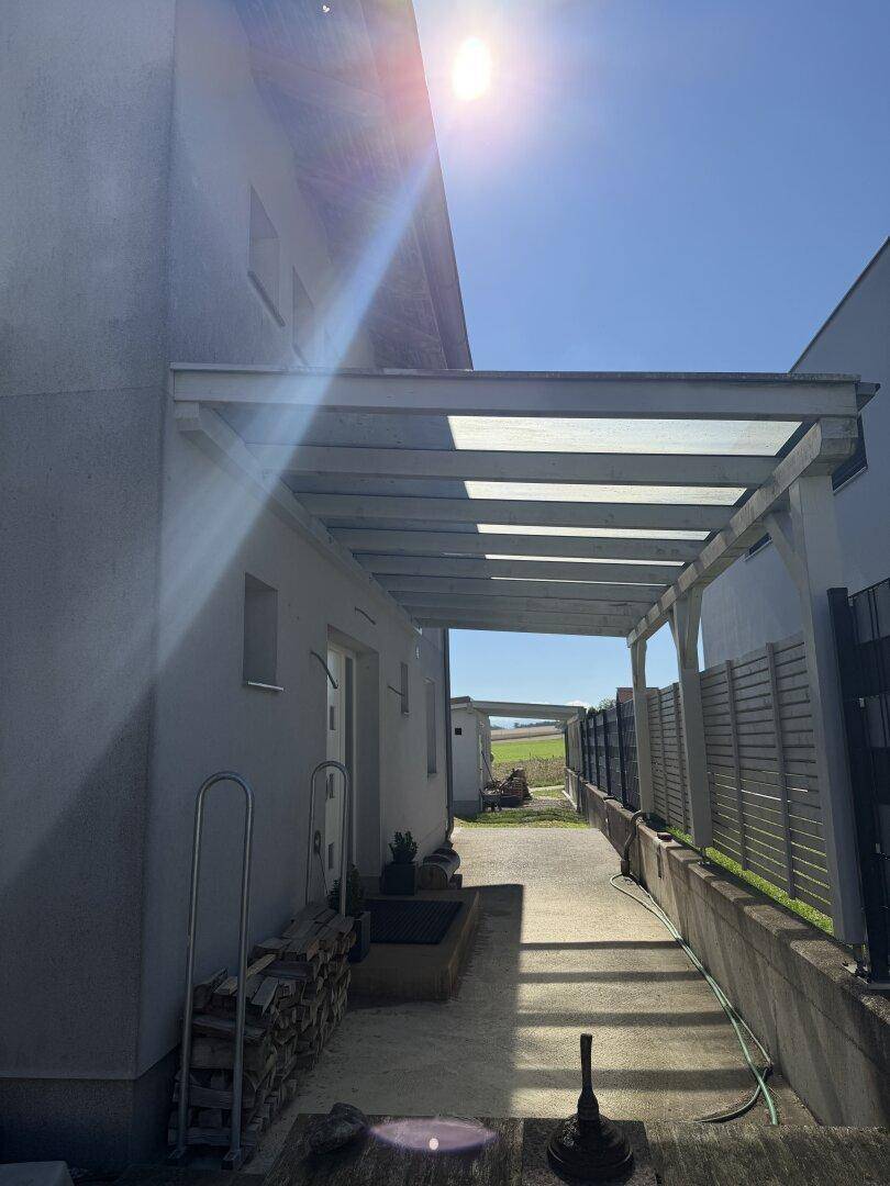 Überdachter Gang neben dem Haus, der zu einem offenen Feld mit Weitblick führt.