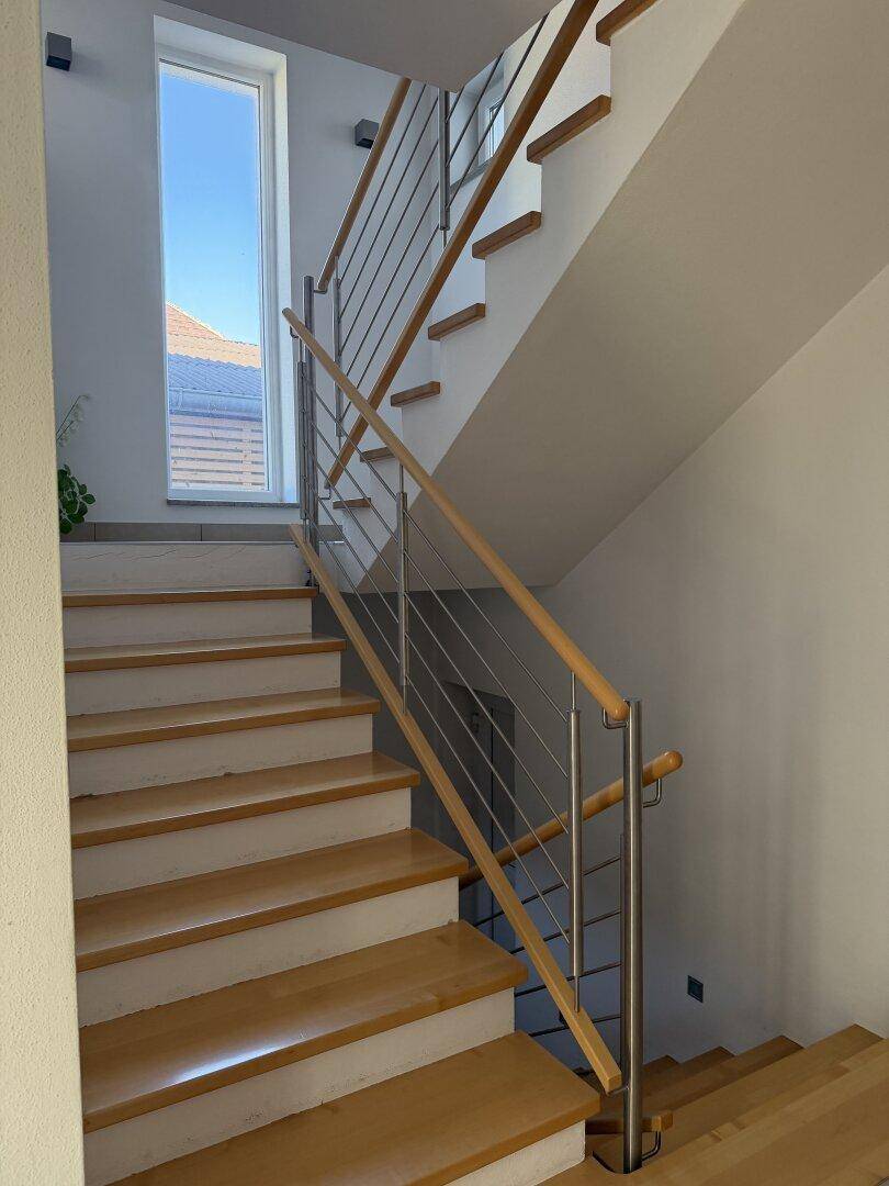 Moderne Holztreppe mit elegantem Edelstahlgeländer, die die oberen Etagen verbindet.