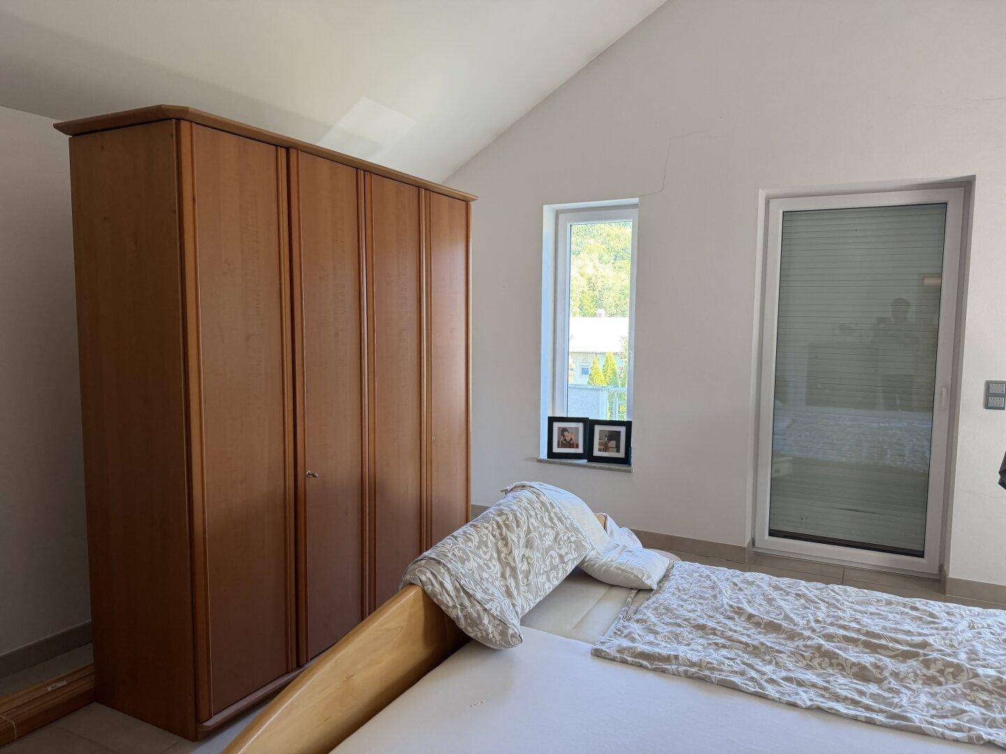 Schlafzimmer mit Holzschrank, Bett und Zugang zu einem Balkon oder einer Terrasse.