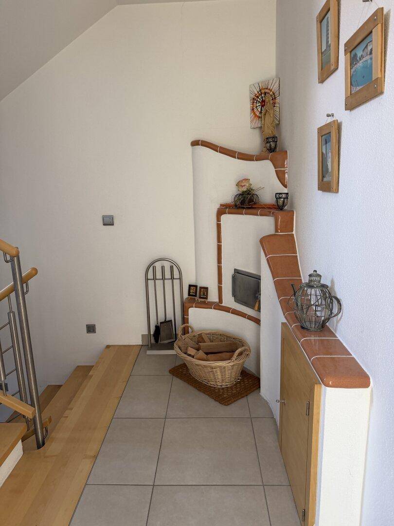 Eingangsbereich mit Fliesenboden, Holztreppe und einem dekorativen Kachelofen.