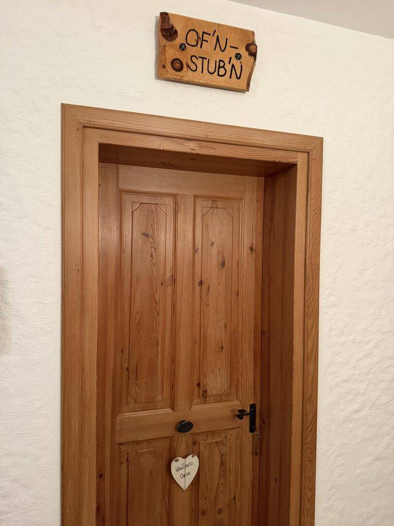 Rustikale Holztür mit handgeschnitztem Schild "OF'N-STUB'N", die zu einem Zimmer führt.