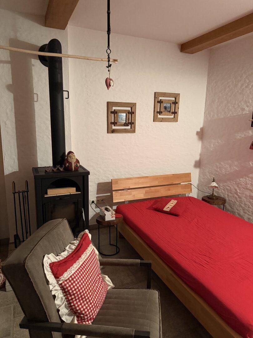 Gemütliches Schlafzimmer im Chalet-Stil mit sichtbaren Holzbalken und einem traditionellen Holzofen.