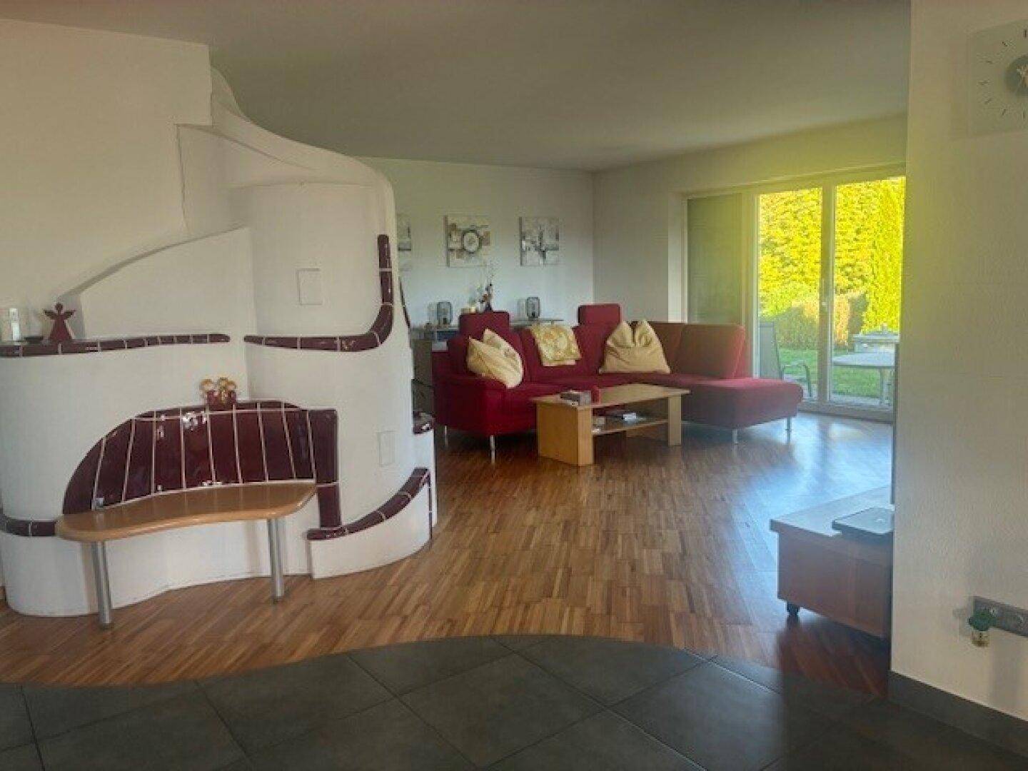 Gemütliches Wohnzimmer mit Holzboden, großem Kachelofen und Zugang zum Garten.