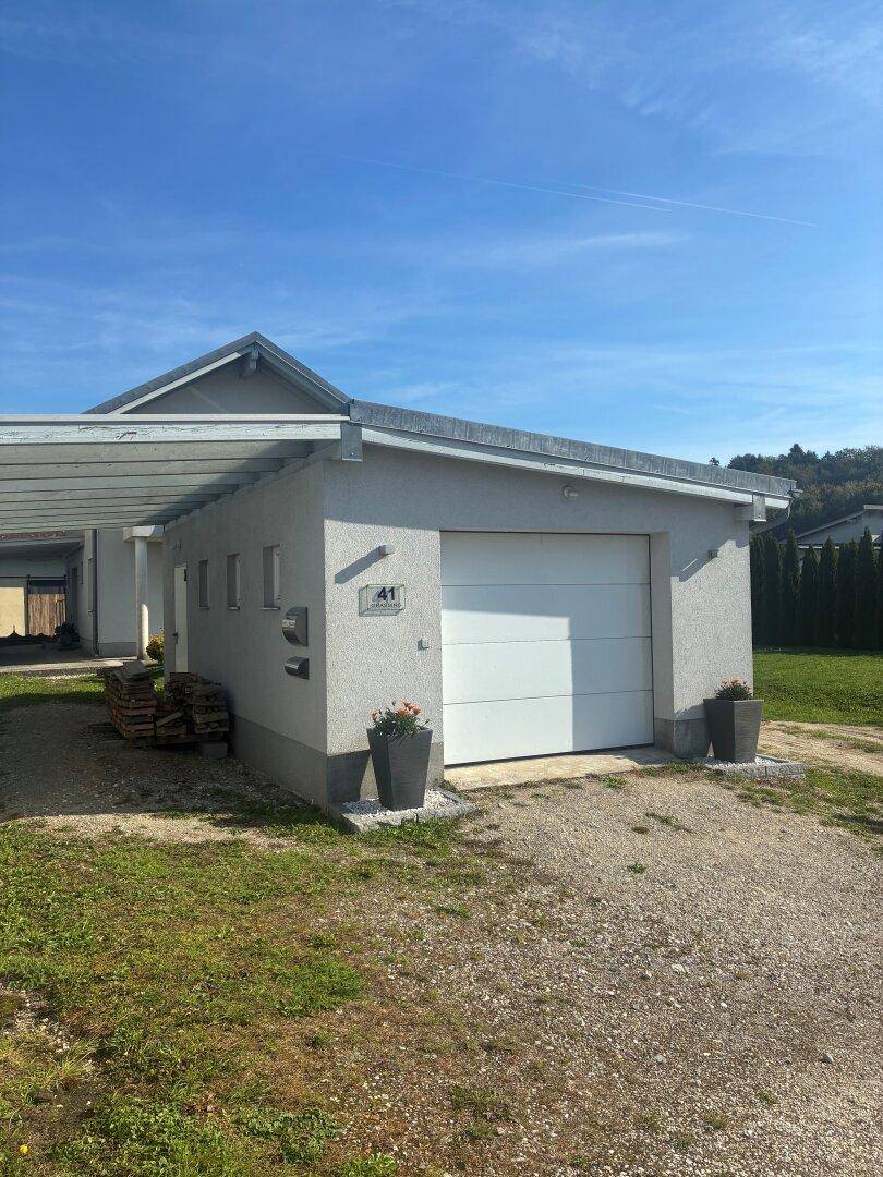 Garage und Carport eines Einfamilienhauses mit Schotterauffahrt und Grünfläche.