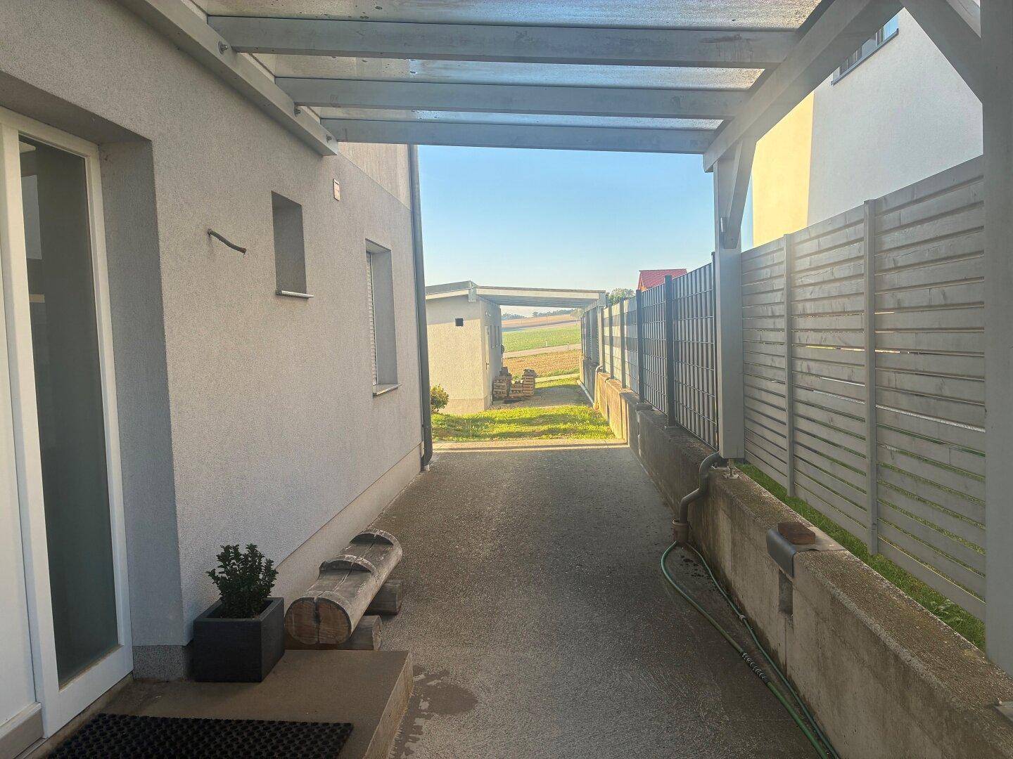 Überdachter Seitenweg des Hauses mit Blick auf die umliegende Landschaft und Felder.