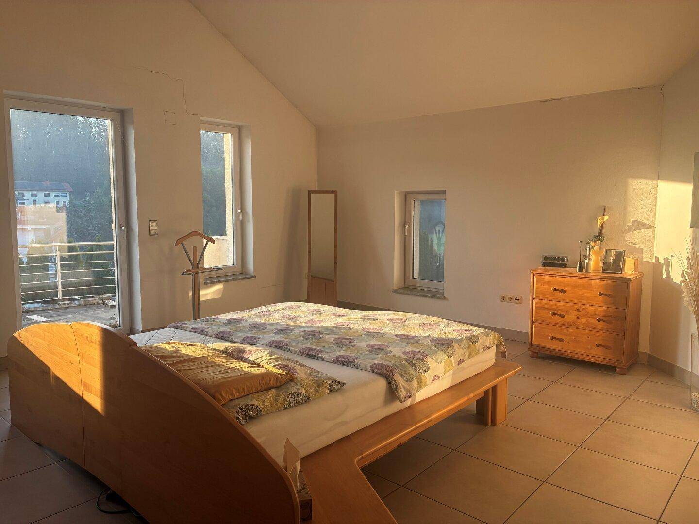 Schlafzimmer mit Holzbett, Fliesenboden und Zugang zu einem sonnigen Balkon.