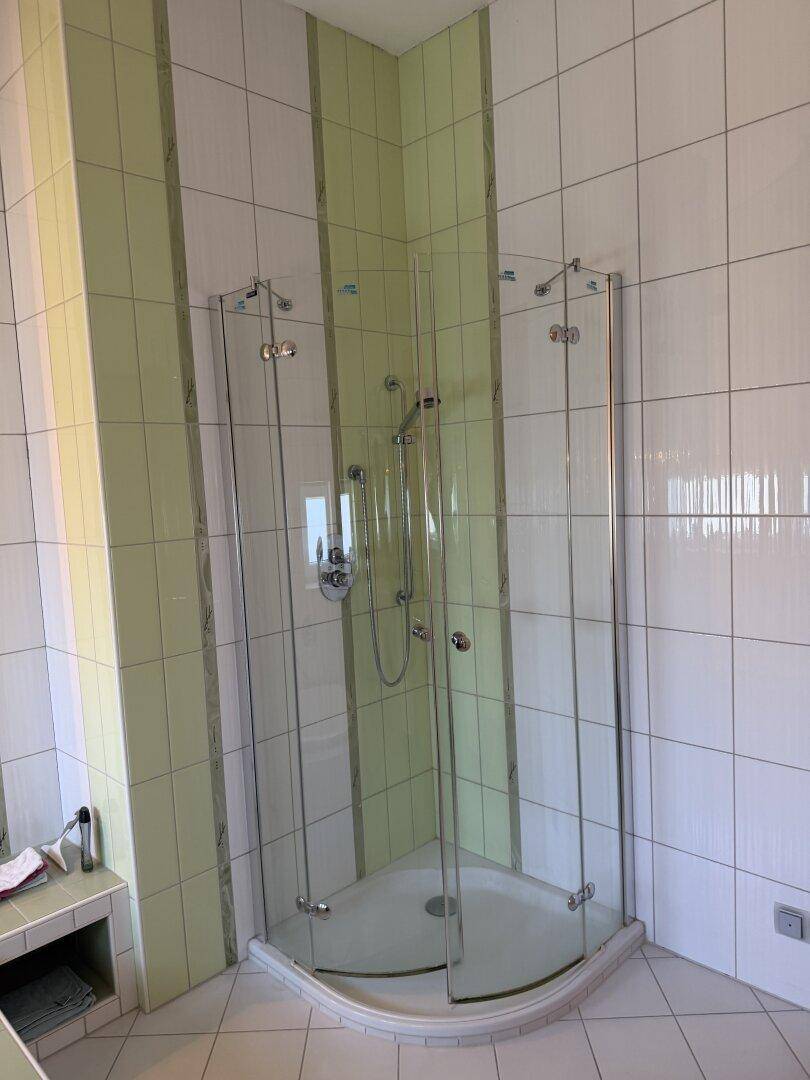 Helle Duschkabine mit Glaswänden und grünen Akzentfliesen in einem Badezimmer.