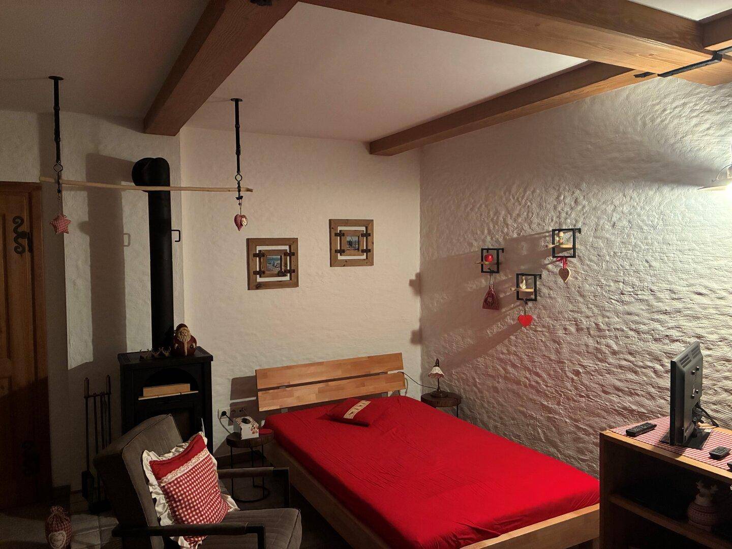 Rustikales Schlafzimmer mit Holzbalken, Steinwand und einem Holzofen für gemütliche Abende.