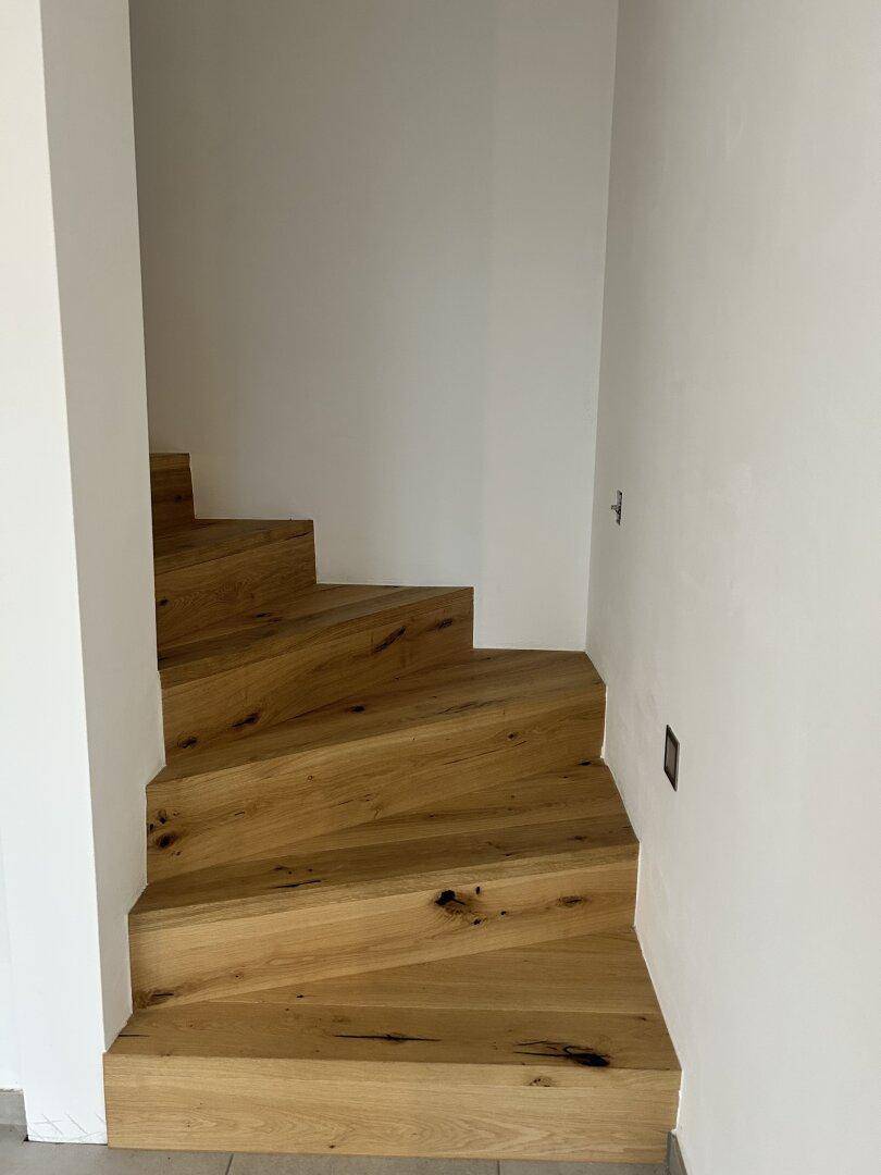 Moderne Holztreppe mit offenen Stufen und natürlicher Maserung in einem hellen Treppenhaus.