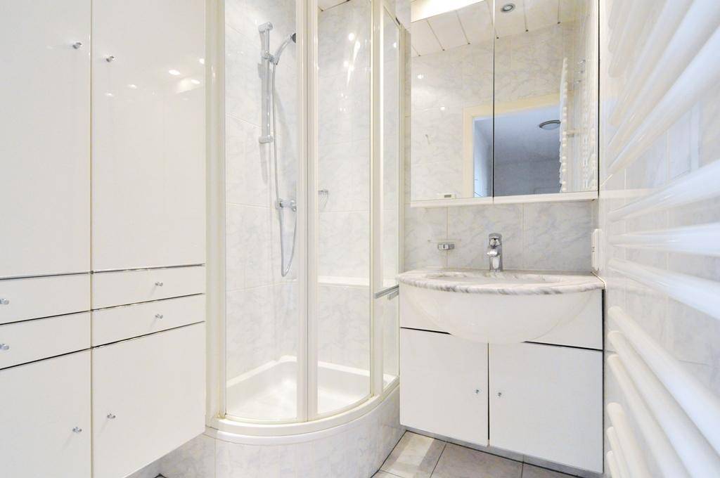Modernes Badezimmer mit Duschkabine, Marmorwaschbecken und weißen Fliesen.