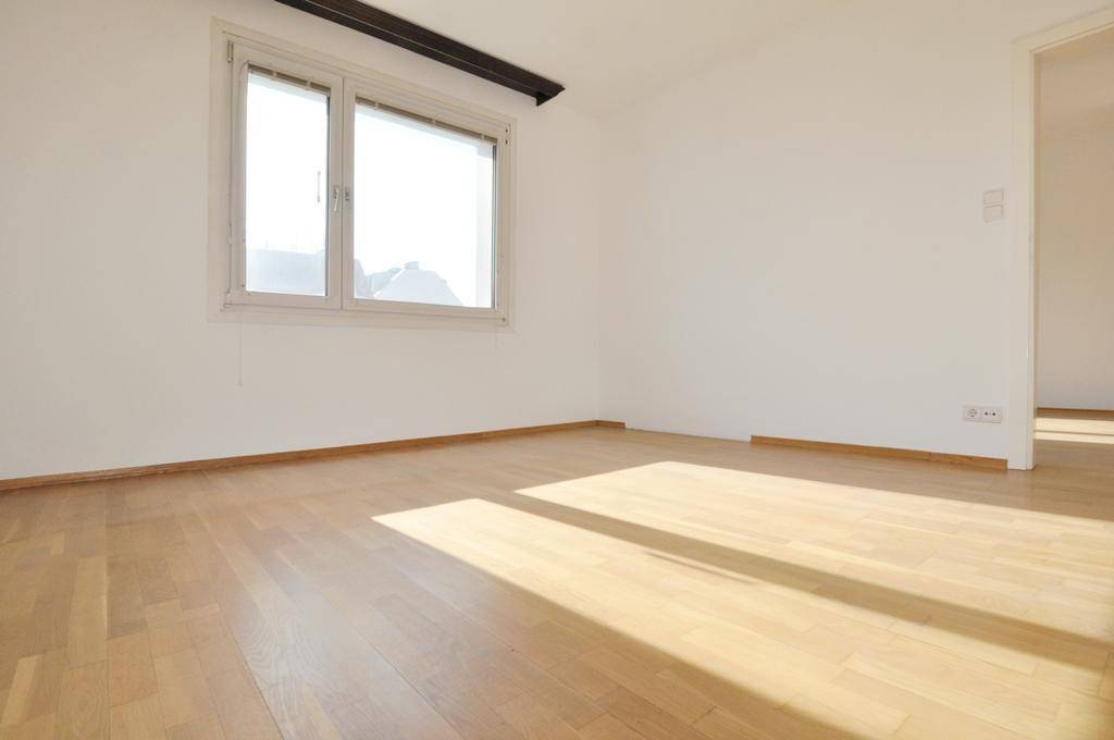 Lichtdurchfluteter Raum mit hellem Parkettboden und offenem Zugang zu einem weiteren Zimmer.