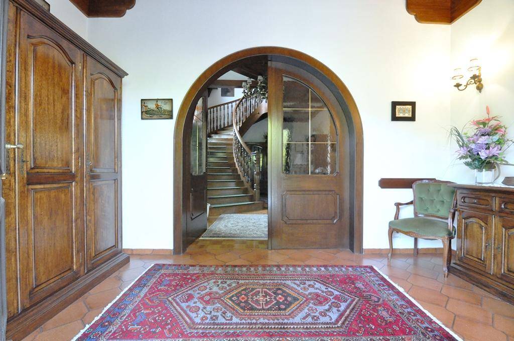 Einladender Eingangsbereich mit Terrakottafliesen, Holztüren und einem Blick auf die geschwungene Treppe.