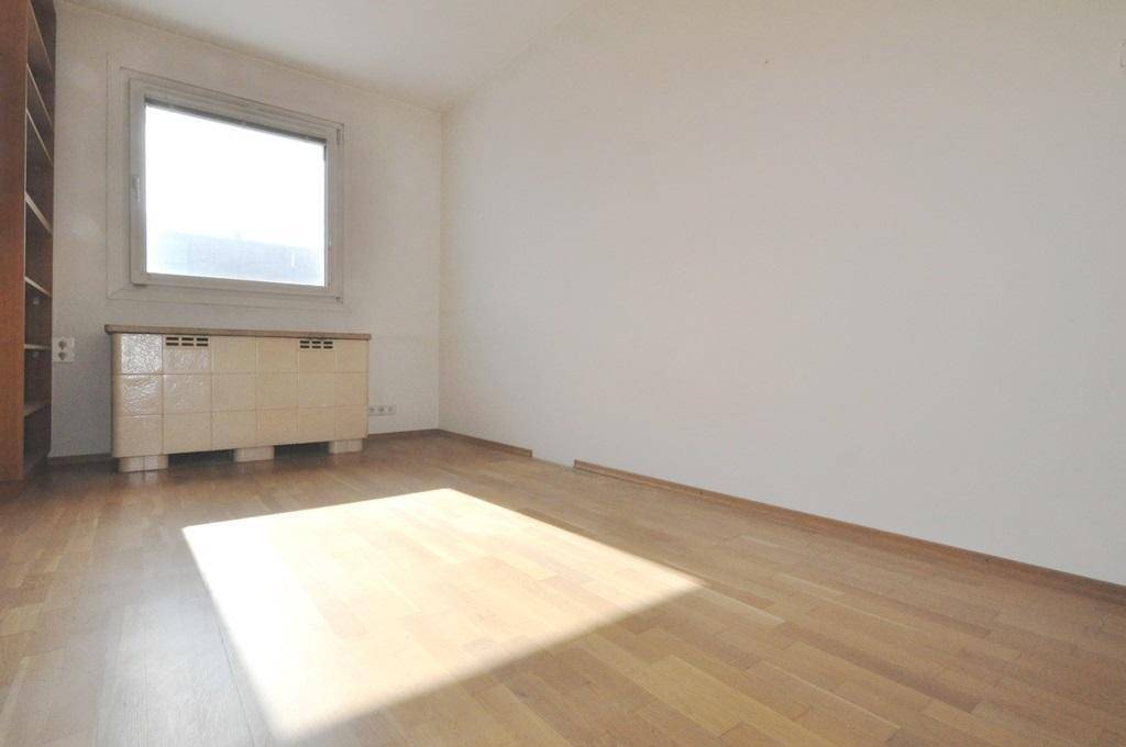 Helles Schlafzimmer mit Parkettboden, großem Fenster und einem Regal an der Wand.