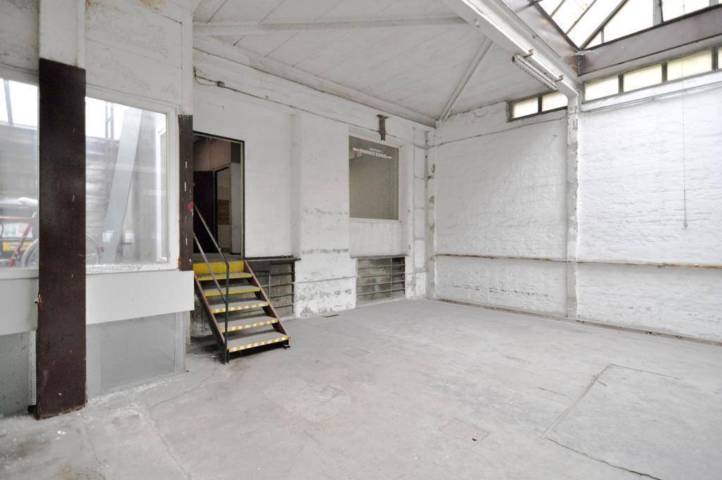 Geräumiger Industrieraum mit hohen Decken, Oberlichtern und einer kleinen Treppe, die zu einem Eingang führt und renoviert werden muss.