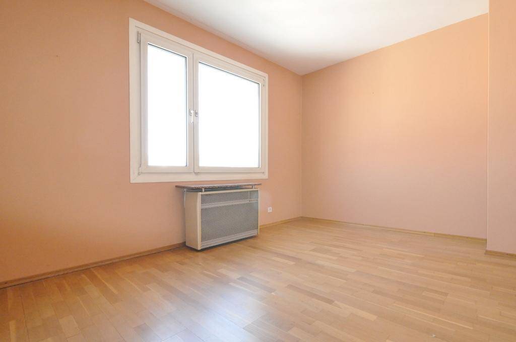 Helles Zimmer mit pfirsichfarbenen Wänden, Parkettboden und einem großen Fenster.