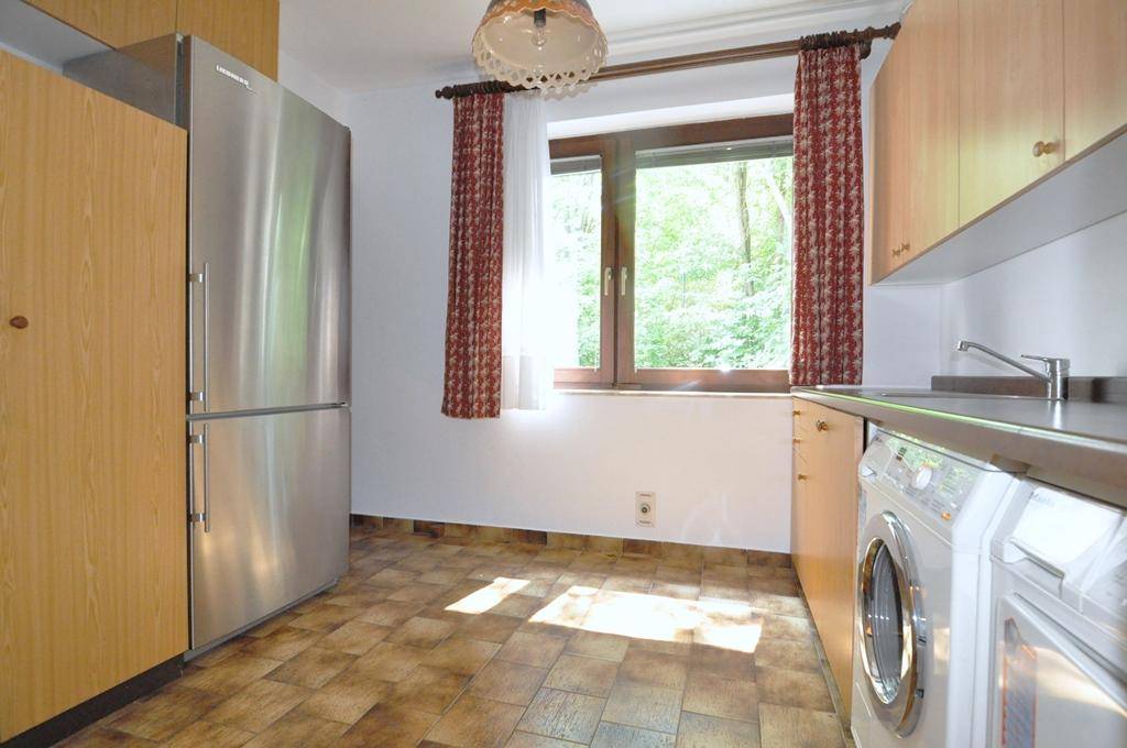 Praktischer Hauswirtschaftsraum mit Kühlschrank, Waschmaschine und Fenster mit Blick ins Grüne.