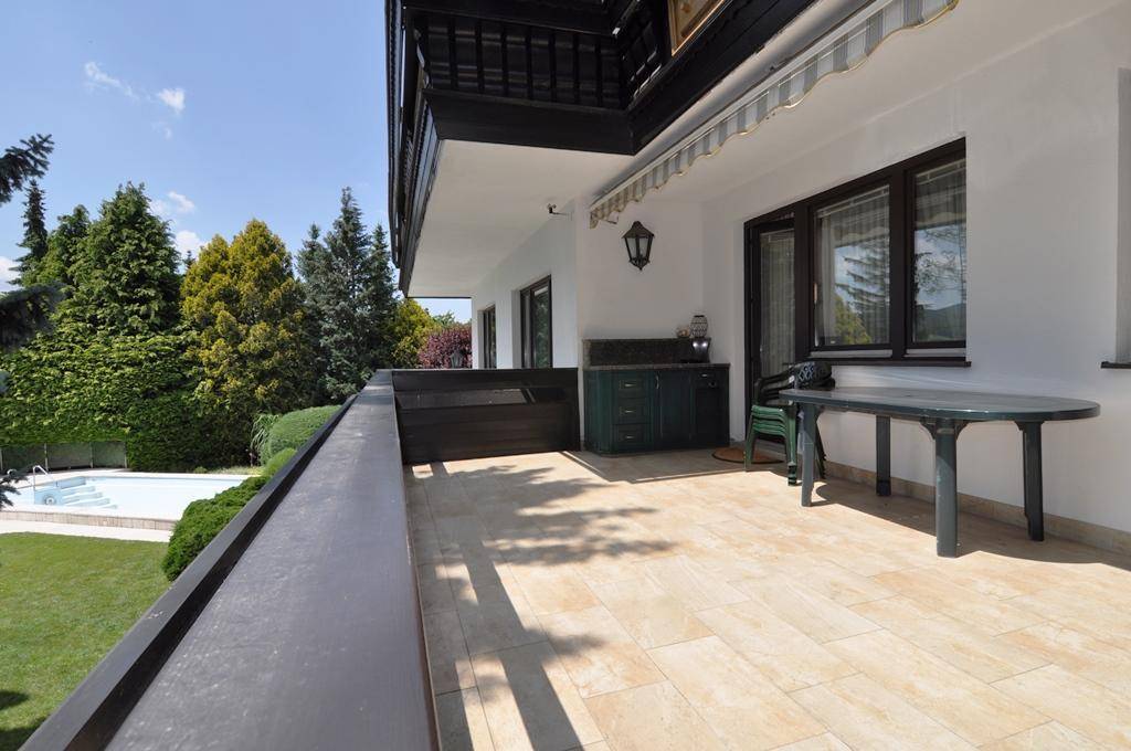 Geräumiger Balkon mit Fliesenboden und Blick auf den Garten mit Swimmingpool.