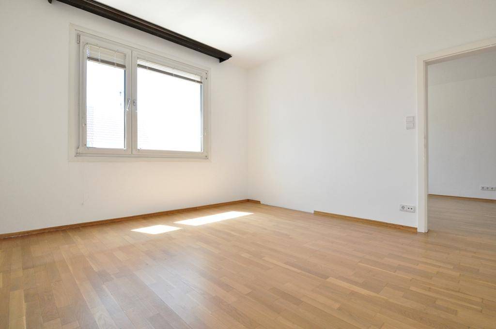 Geräumiges Zimmer mit hellem Parkettboden und einem Fenster, das den Raum erhellt.