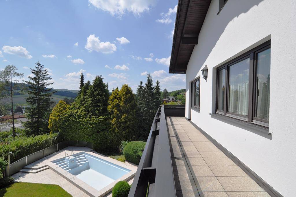 Langer Balkon mit Fliesenboden und weitem Blick über den Pool und die umliegende Landschaft.
