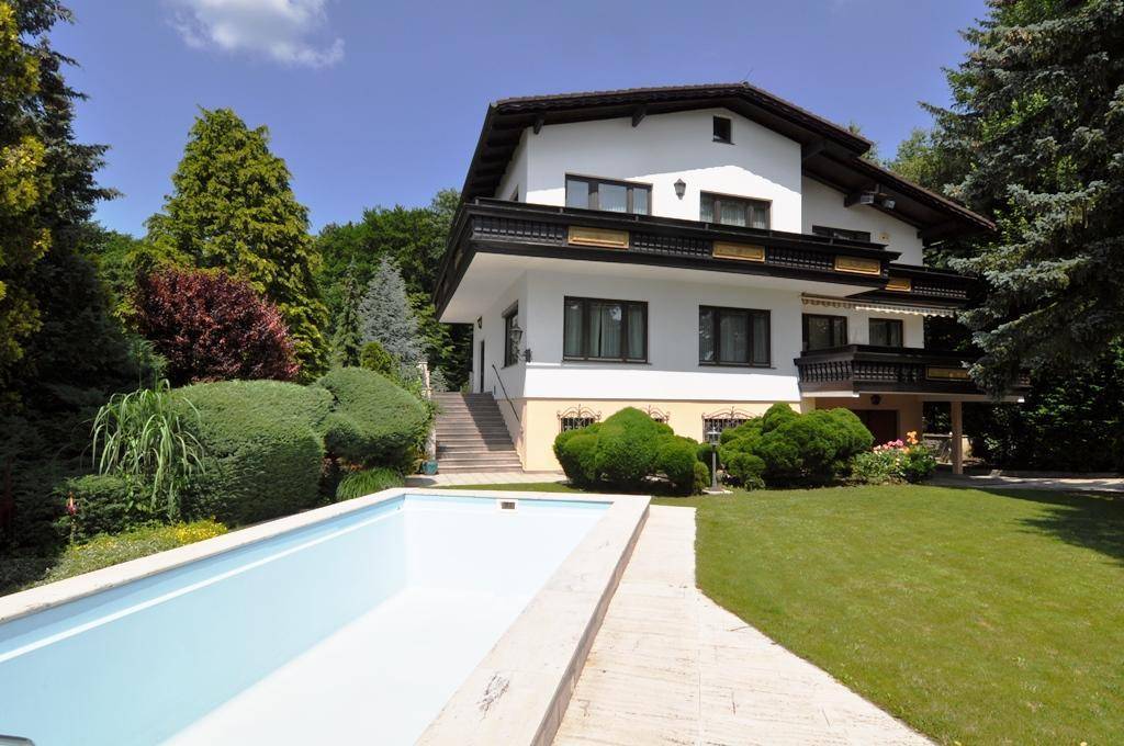 Elegantes Haus mit traditioneller Architektur, umgeben von einem weitläufigen Garten mit Swimmingpool.