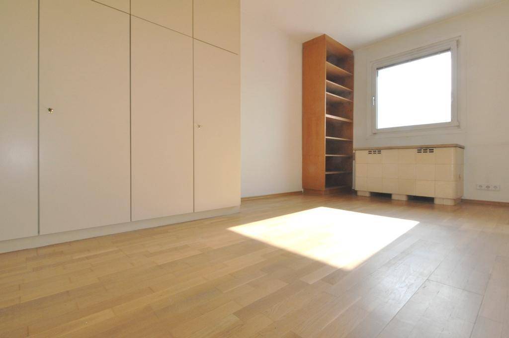 Schlafzimmer mit Einbauschränken, Holzregal und hellem Parkettboden, beleuchtet von Sonnenlicht.