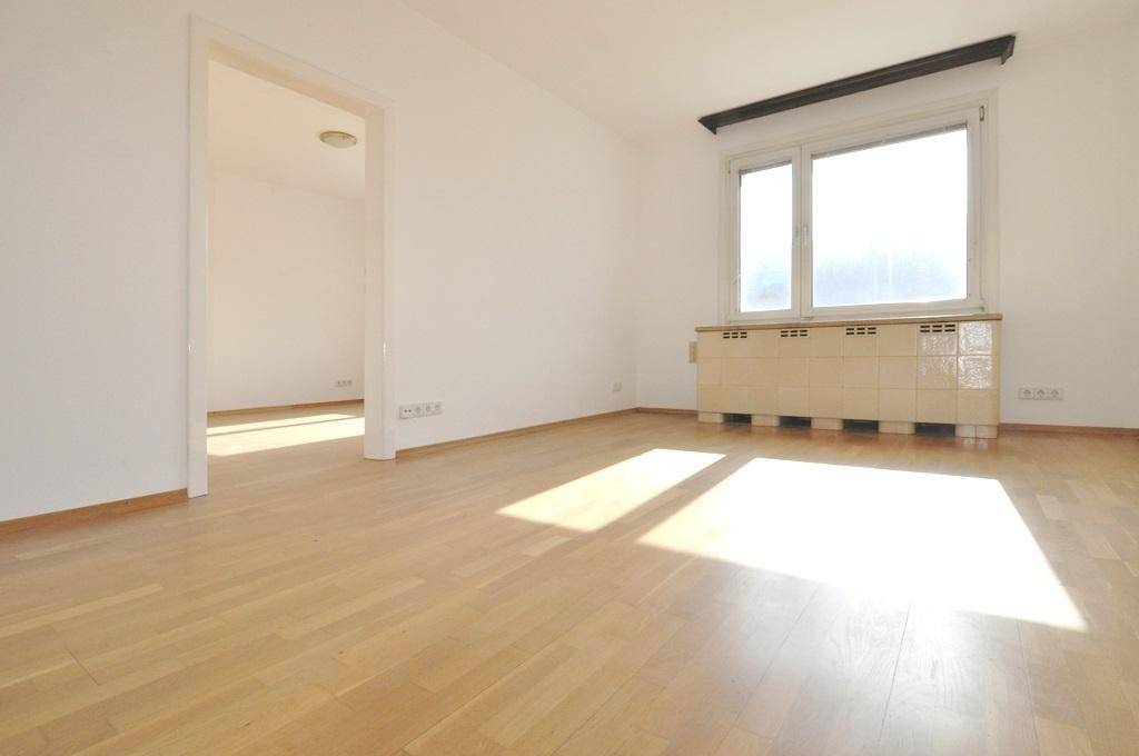 Heller Wohnraum mit Parkettboden, Fenster und einem gefliesten Heizkörper unter der Fensterbank.