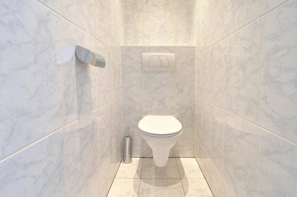 Separates WC mit wandhängender Toilette und weißen Fliesen an den Wänden.