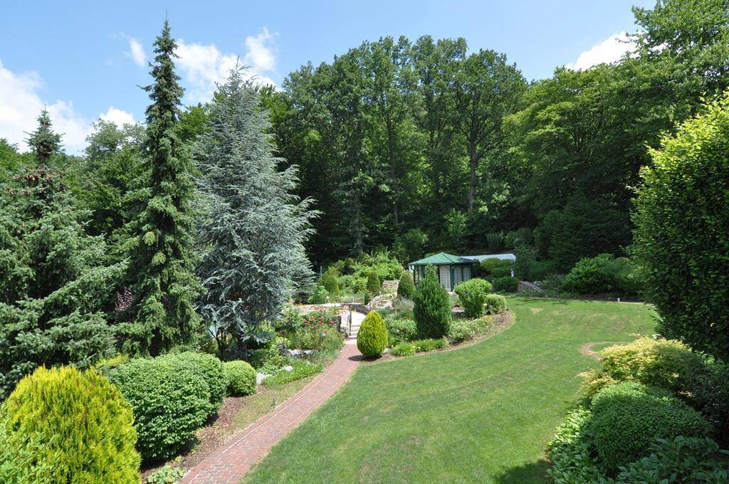 Weitläufiger, parkähnlicher Garten mit geschwungenen Wegen, hohen Bäumen und gepflegten Grünflächen.